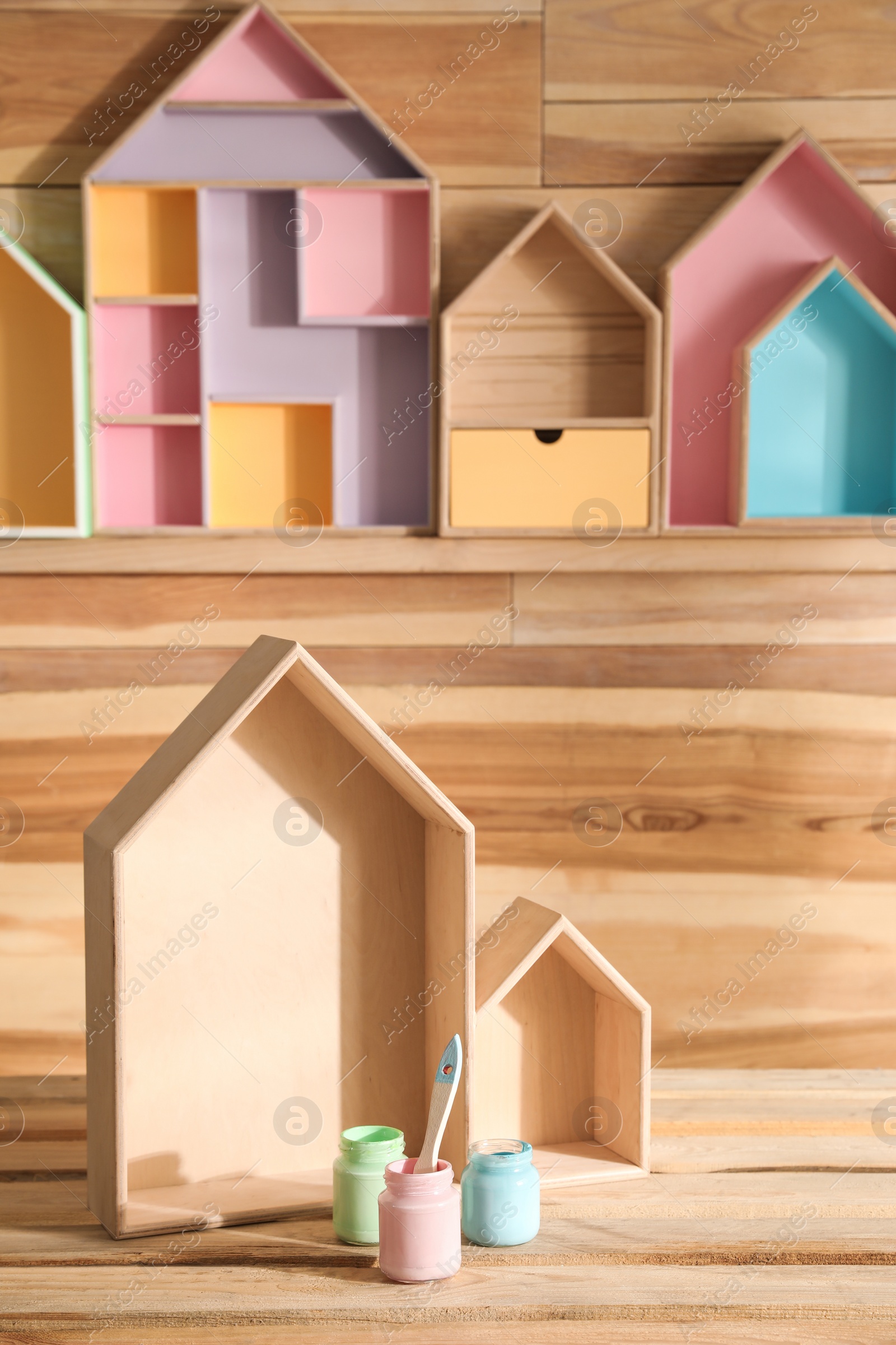 Photo of House shaped shelves, jars of paints and brush on wooden table. Interior elements