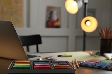 Photo of Artist's workplace with soft pastels, laptop and drawing pencils on table indoors
