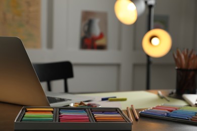 Artist's workplace with soft pastels, laptop and drawing pencils on table indoors