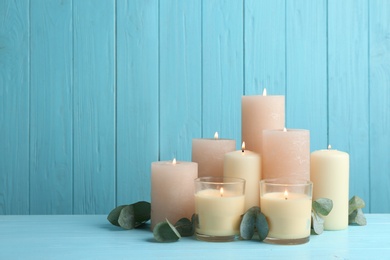 Set of burning candles with eucalyptus on table against light blue wooden background. Space for text