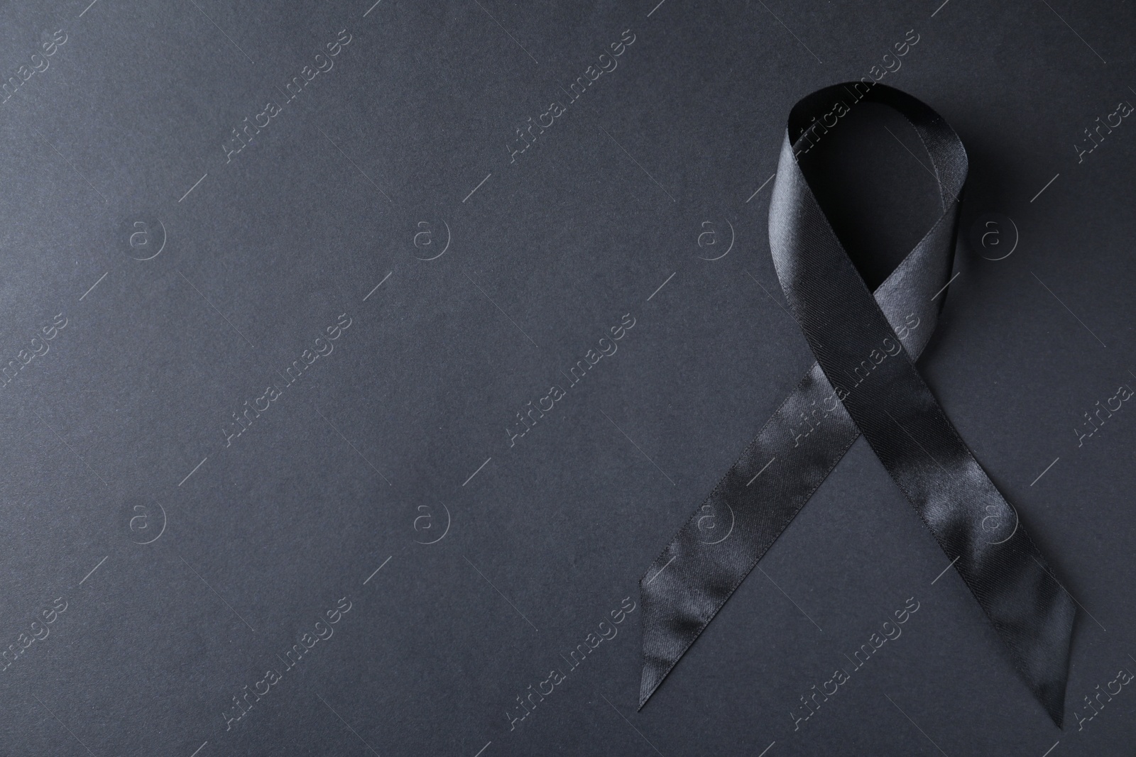 Photo of Black ribbon on dark background, top view with space for text. Funeral symbol