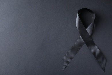 Photo of Black ribbon on dark background, top view with space for text. Funeral symbol