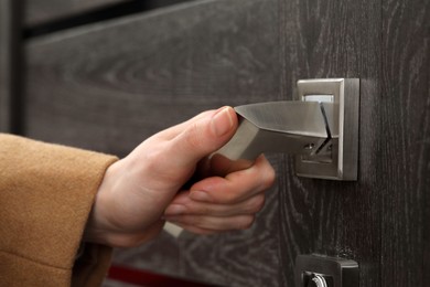 Photo of Woman opening wooden door indoors, closeup of hand on handle