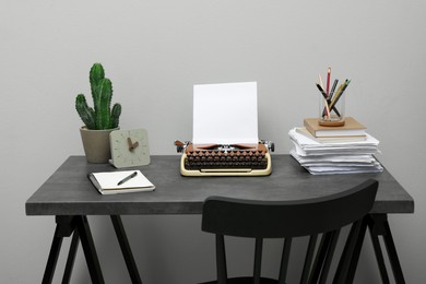 Typewriter and stack of papers on dark table near light grey wall. Writer's workplace