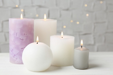 Set of different candles burning on white table