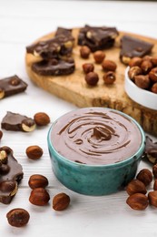 Bowl with tasty paste, chocolate pieces and nuts on white wooden table