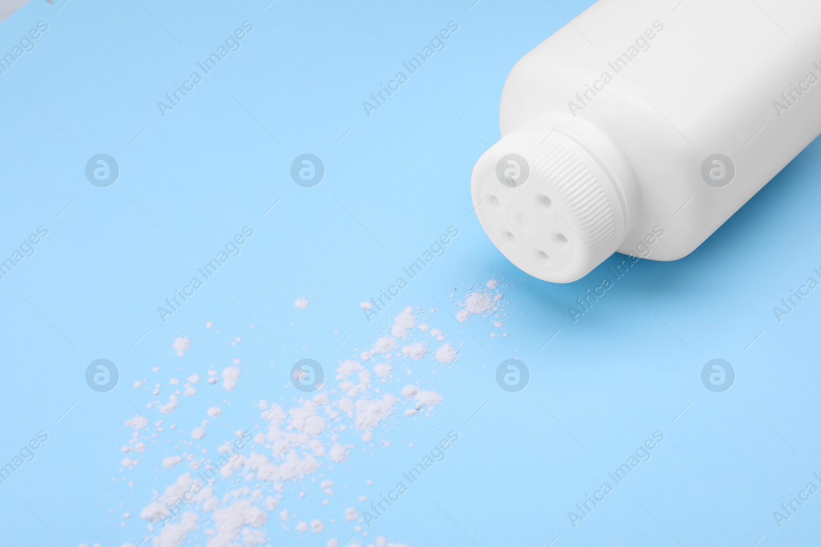Photo of Bottle and scattered dusting powder on light blue background. Baby cosmetic product