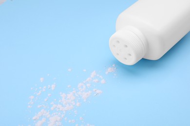 Bottle and scattered dusting powder on light blue background. Baby cosmetic product