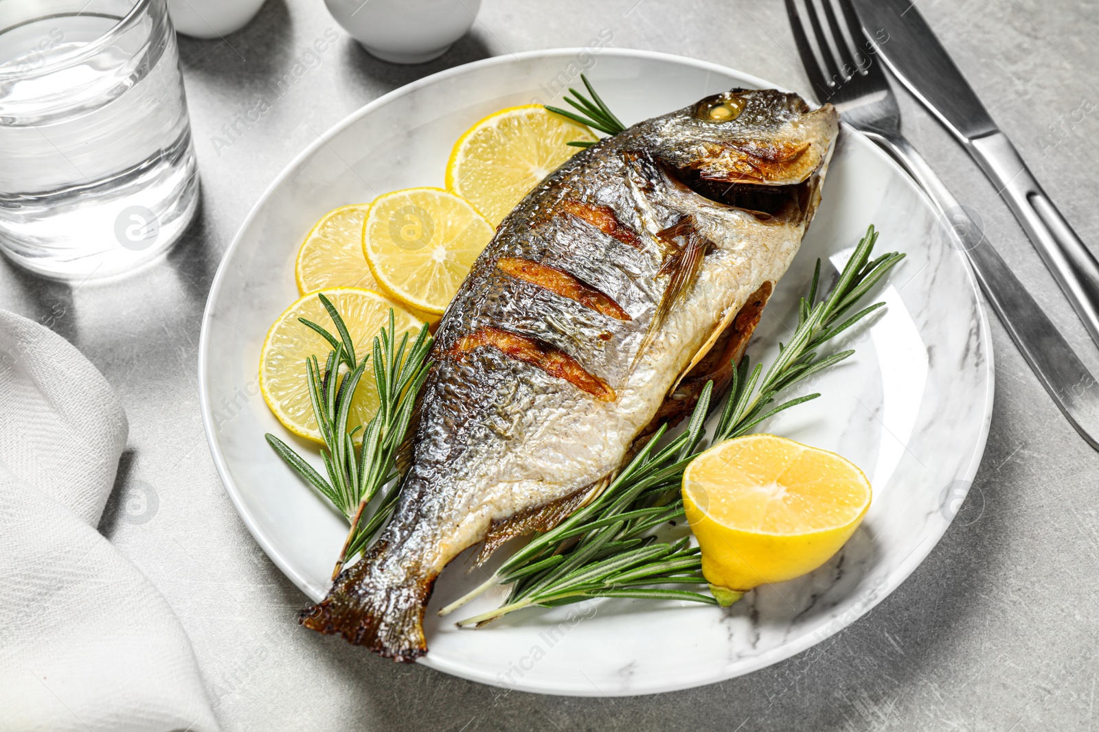 Photo of Delicious roasted fish with lemon on grey table