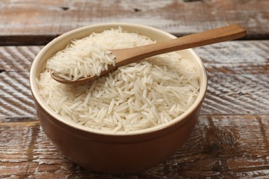 Photo of Raw basmati rice and spoon in bowl on wooden table, closeup