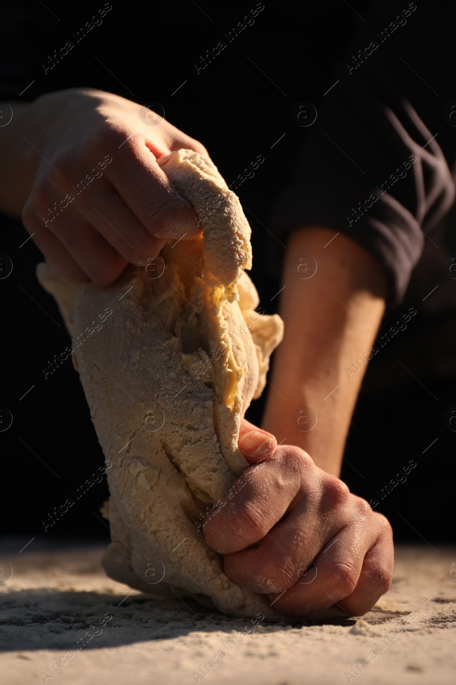 Photo of Making bread. Woman kneading dough at table on dark background, closeup