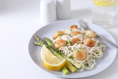 Delicious scallop pasta with asparagus, green onion and lemon served on white table, closeup