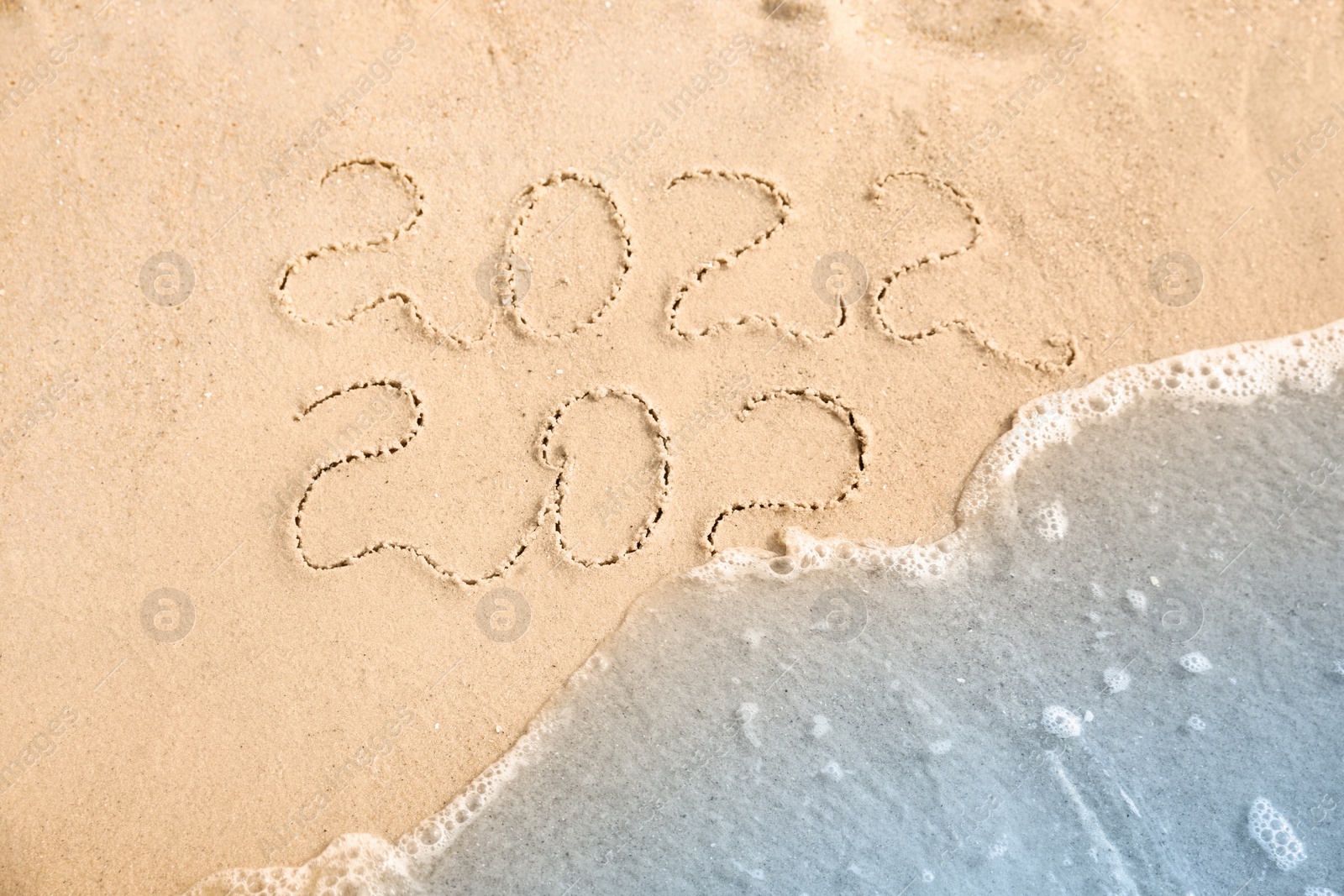 Photo of Dates written on sandy beach. 2021 washed by sea wave as New 2022 Year coming, top view