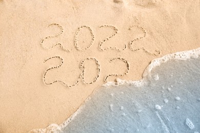 Photo of Dates written on sandy beach. 2021 washed by sea wave as New 2022 Year coming, top view