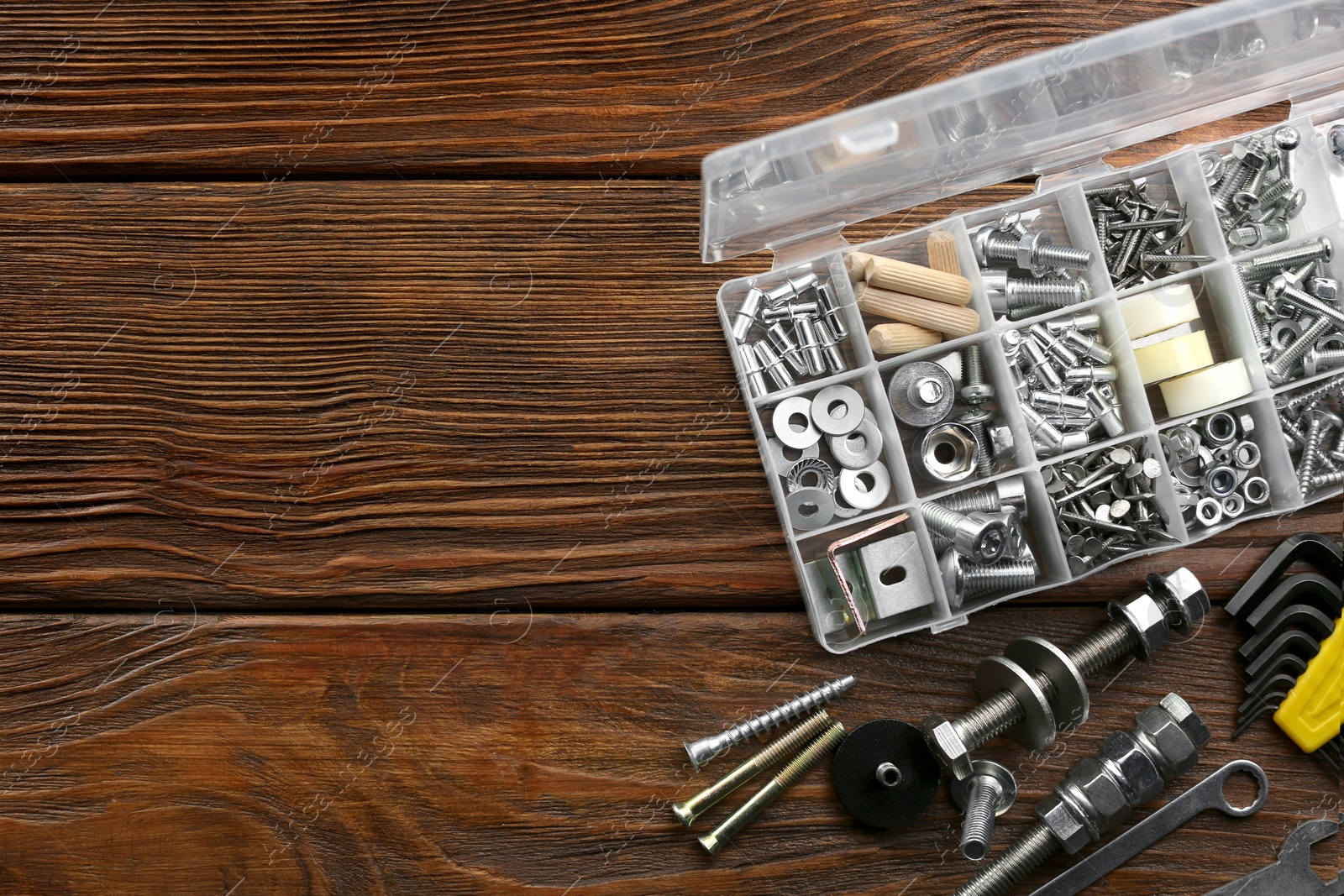 Photo of Plastic box with different furniture fittings and tools on wooden table, flat lay. Space for text