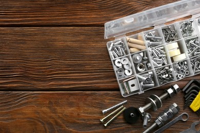 Photo of Plastic box with different furniture fittings and tools on wooden table, flat lay. Space for text