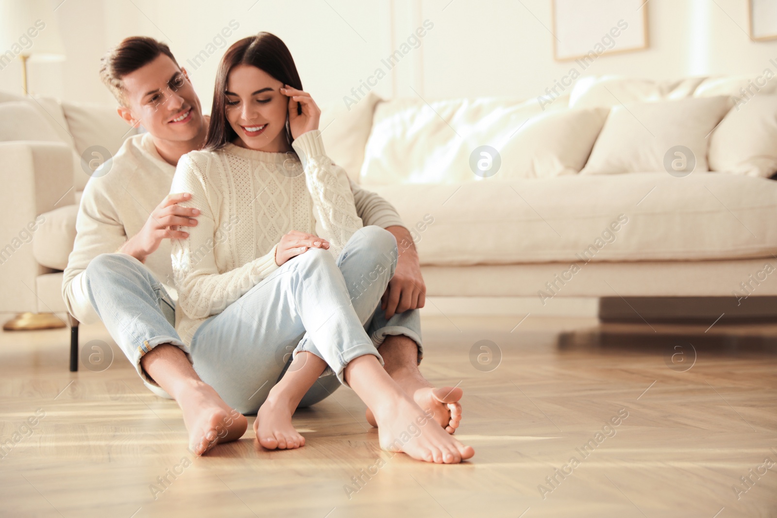 Photo of Happy couple sitting on warm floor in living room. Heating system