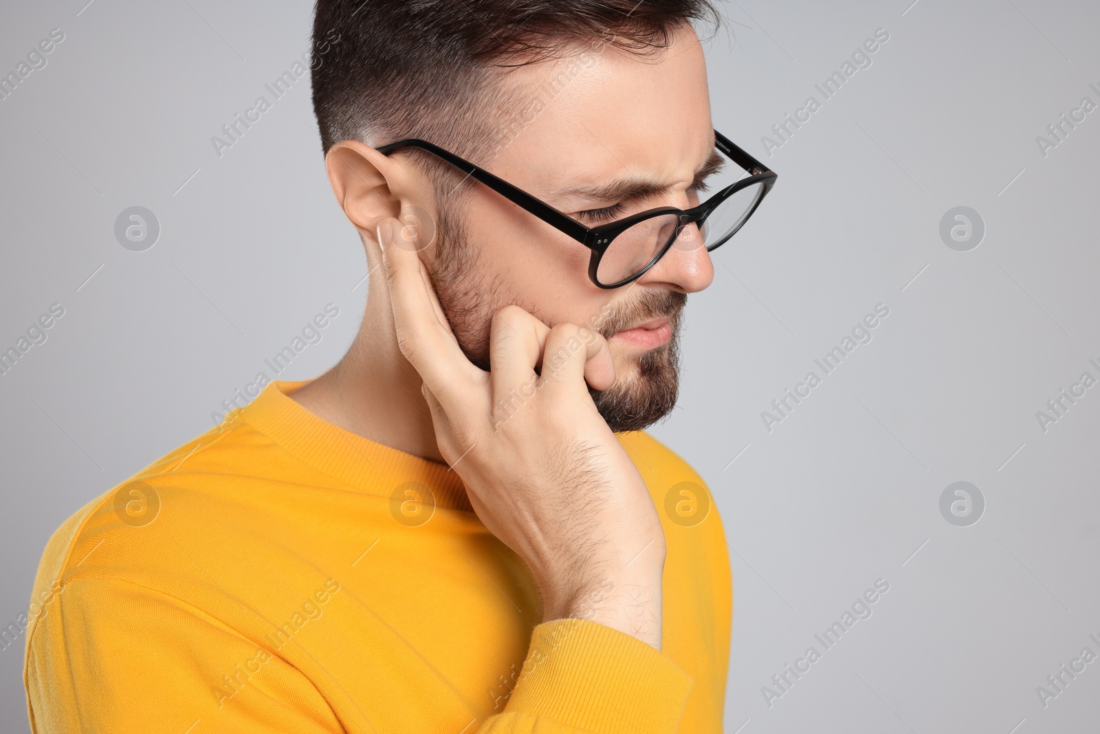 Photo of Young man suffering from ear pain on light grey background