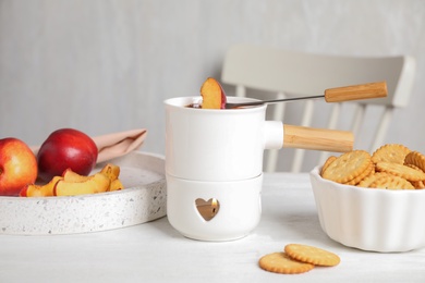 Fondue pot with chocolate and peach on white wooden table in kitchen