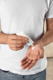 Photo of Man applying cream from tube onto hand indoors, closeup