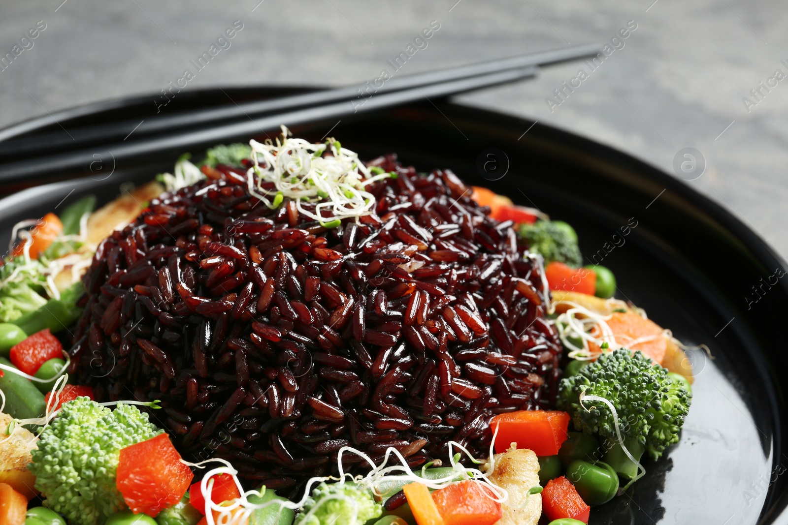 Photo of Plate with cooked brown rice and chopsticks, closeup