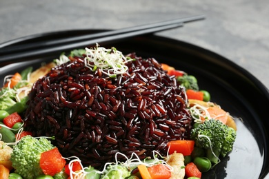 Plate with cooked brown rice and chopsticks, closeup