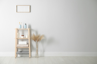 Photo of Wooden shelving unit with toiletries near white wall indoors, space for text. Bathroom interior element