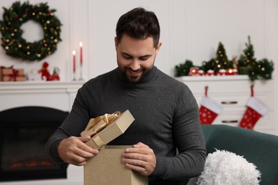 Photo of Happy young man opening Christmas gift at home