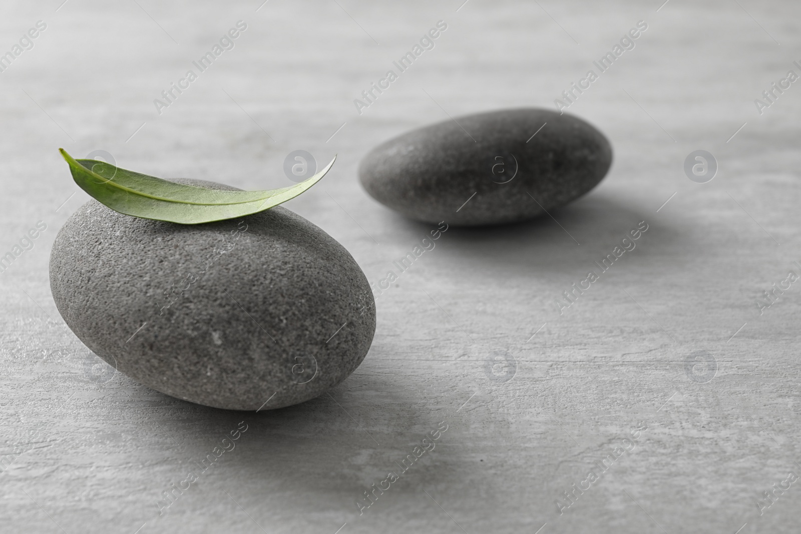 Photo of Spa stones with green leaf on grey background. Space for text