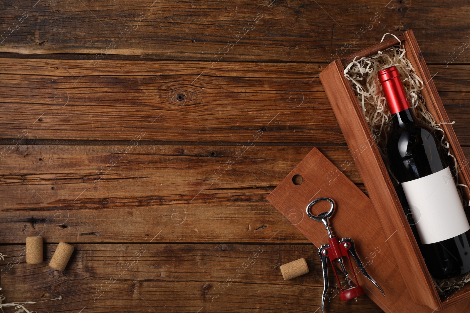 Photo of Box with wine bottle, corkscrew and corks on wooden table, flat lay. Space for text