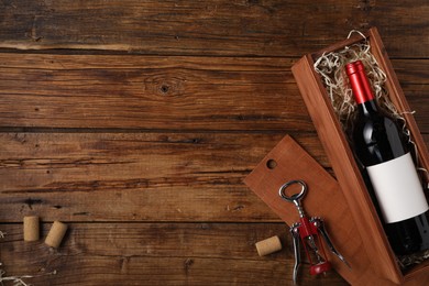 Photo of Box with wine bottle, corkscrew and corks on wooden table, flat lay. Space for text