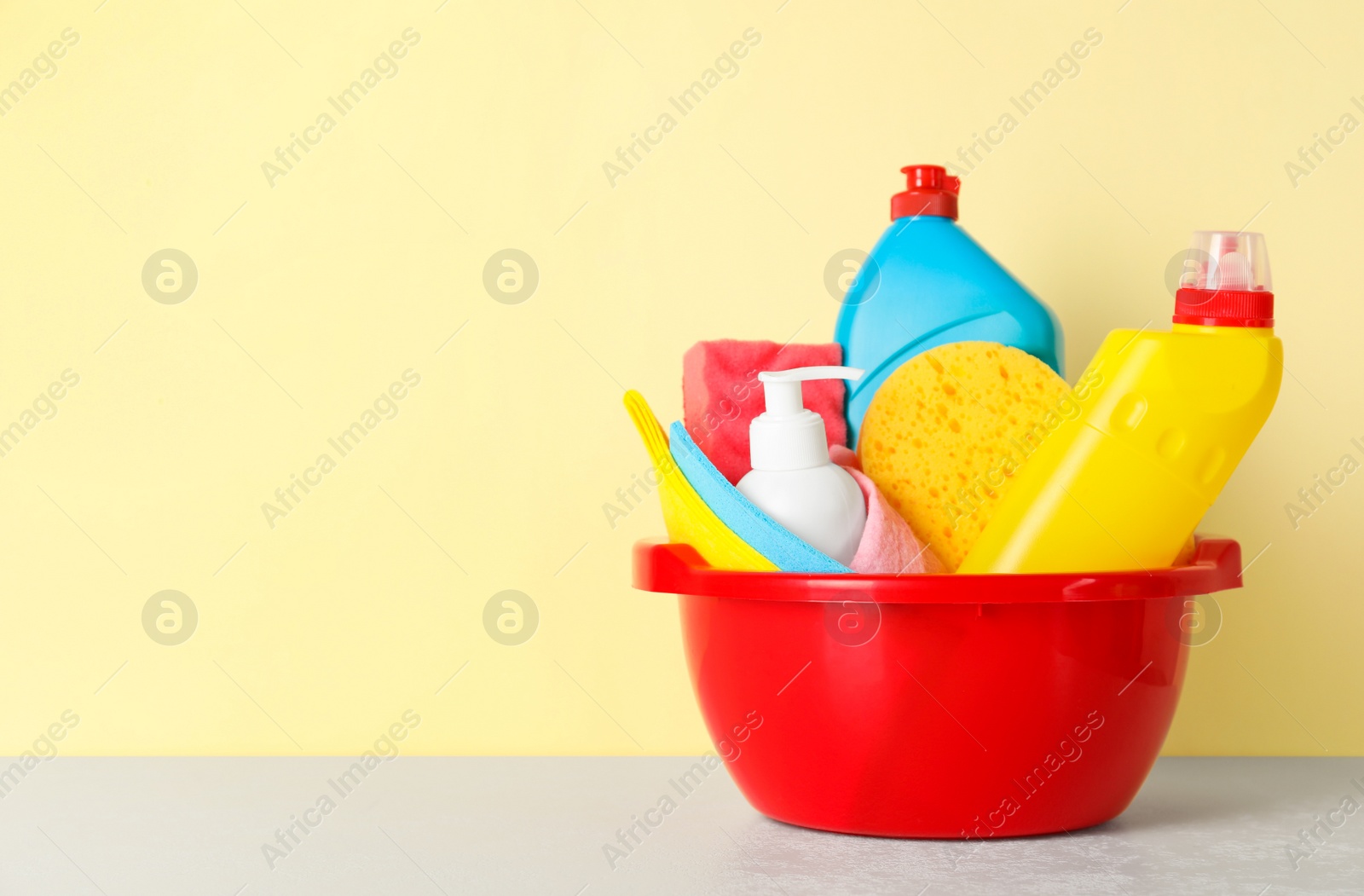 Photo of Basin with different cleaning supplies on light floor near beige wall. Space for text