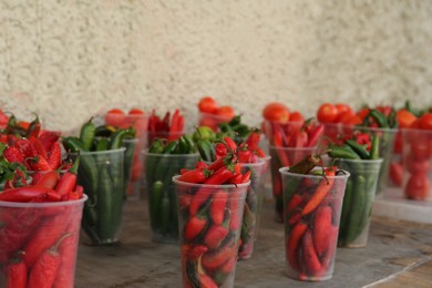 Photo of Many plastic cups with fresh chilli peppers on grey counter at market