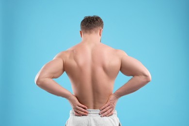 Photo of Man suffering from back pain on light blue background, back view
