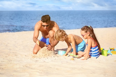 Father and children playing on sandy beach near sea. Summer holidays with family