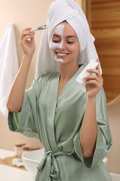 Photo of Woman applying face mask in bathroom. Spa treatments