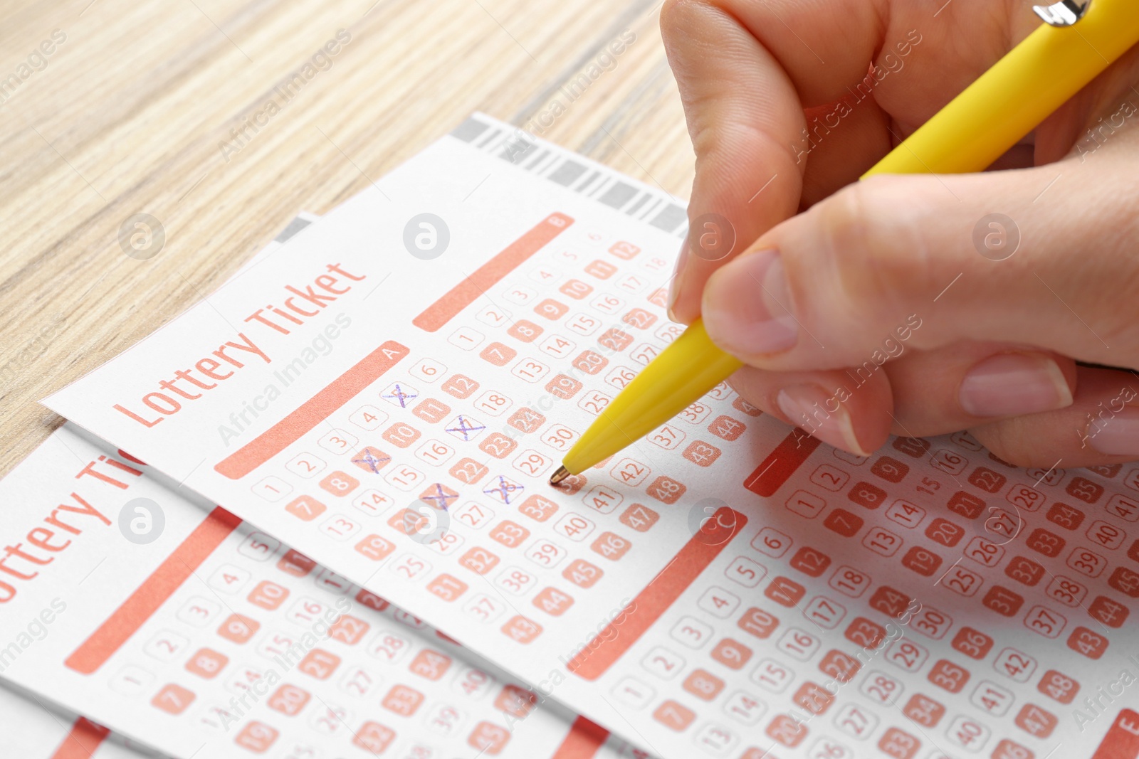 Photo of Woman filling out lottery tickets with pen on wooden table, closeup. Space for text