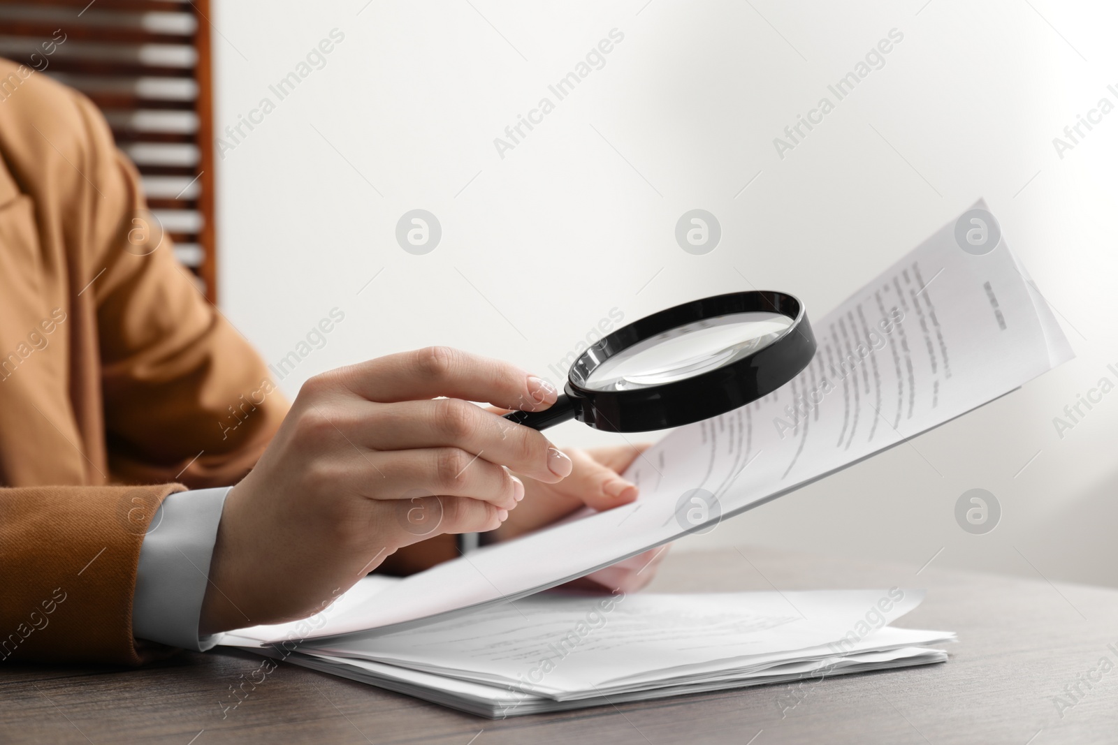 Photo of Woman looking at document through magnifier at table indoors, closeup. Searching concept