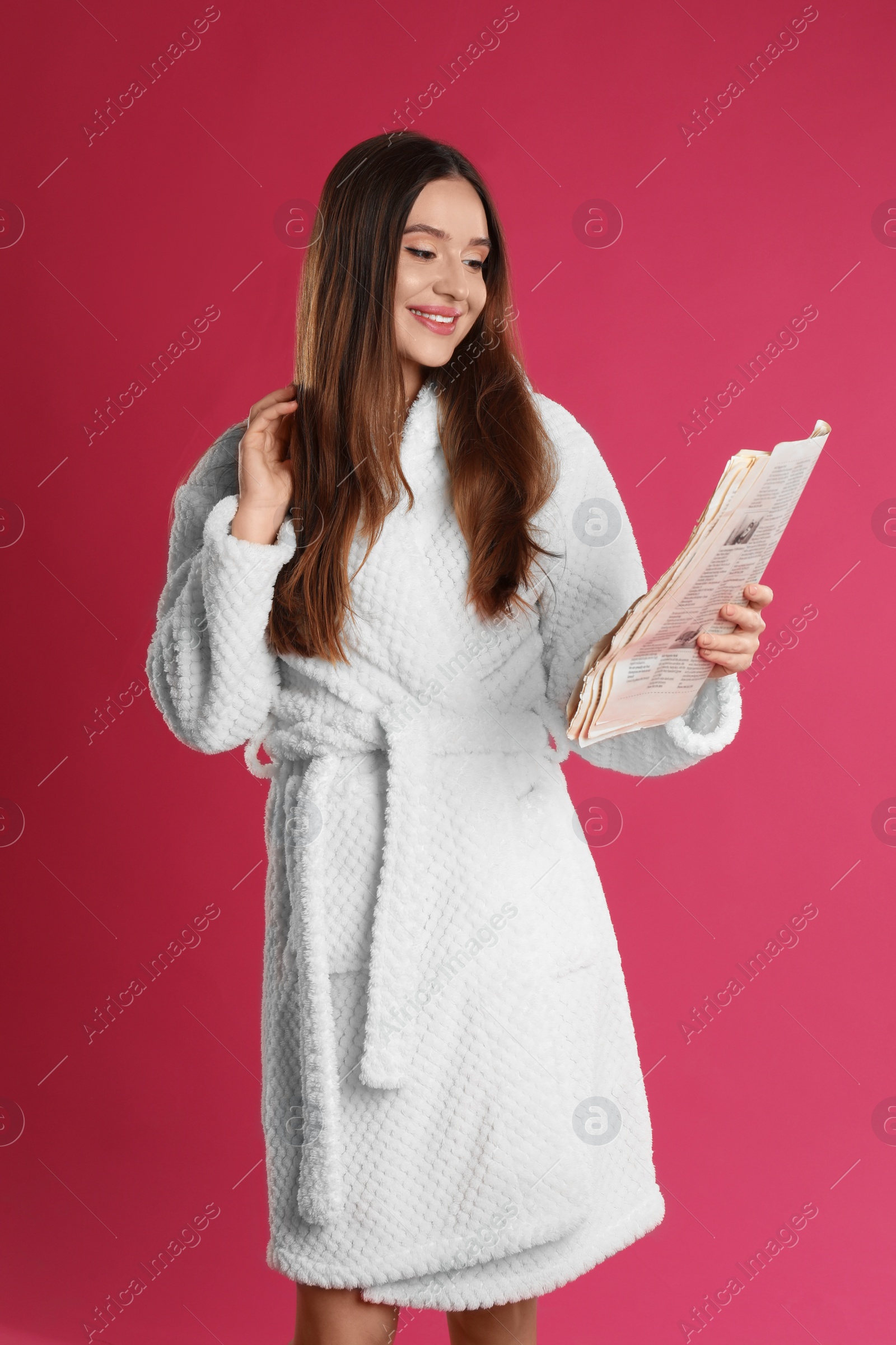 Photo of Beautiful young woman in bathrobe reading newspaper on crimson background