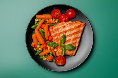 Tasty grilled salmon with mixed vegetables on green background, top view