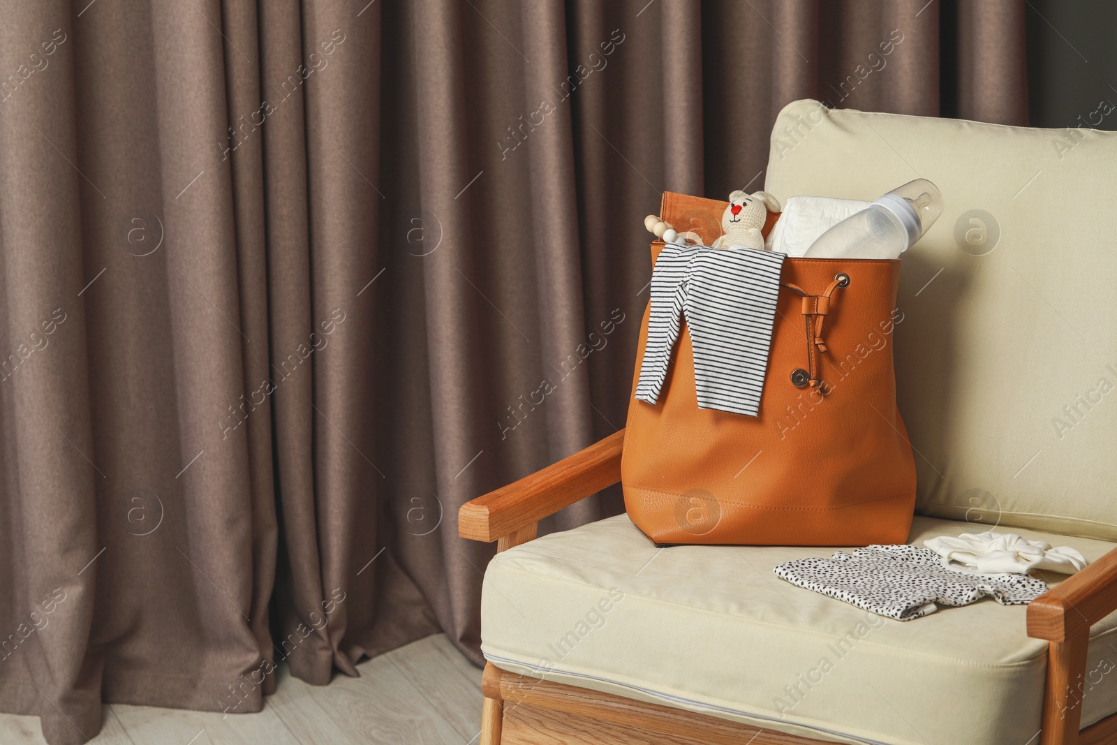 Photo of Mother's bag with baby's stuff on armchair indoors. Space for text