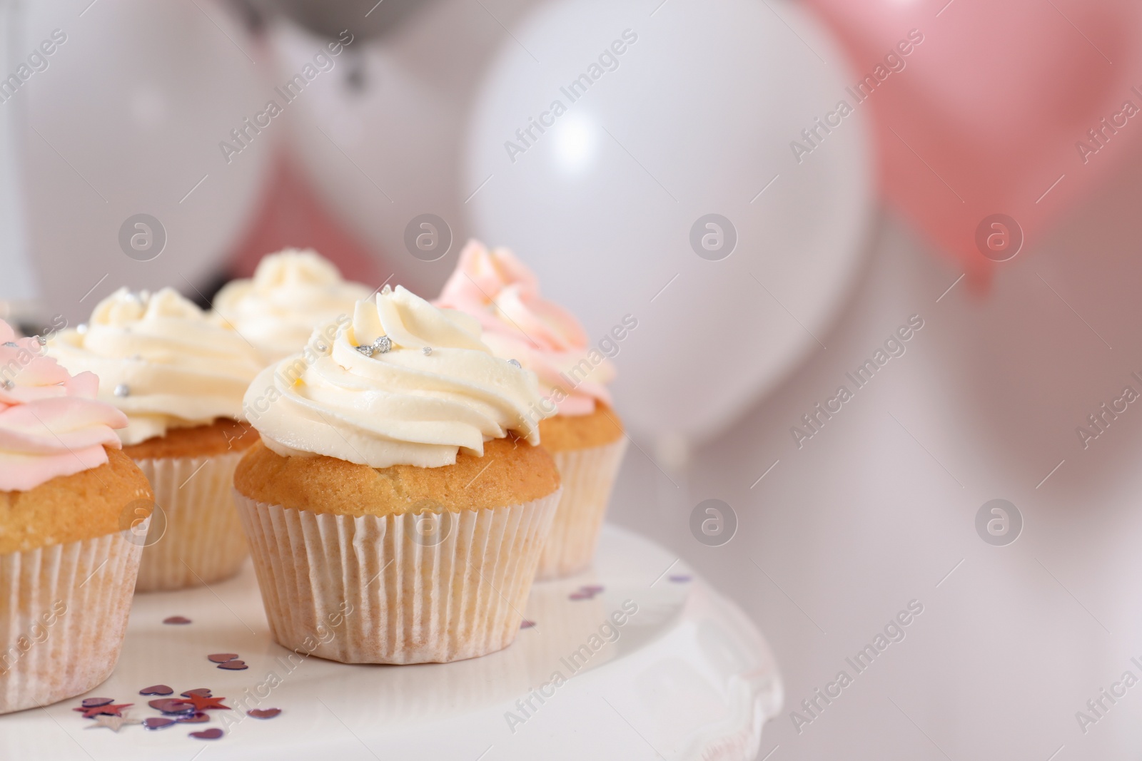 Photo of Stand with cupcakes and blurred balloons on background, closeup