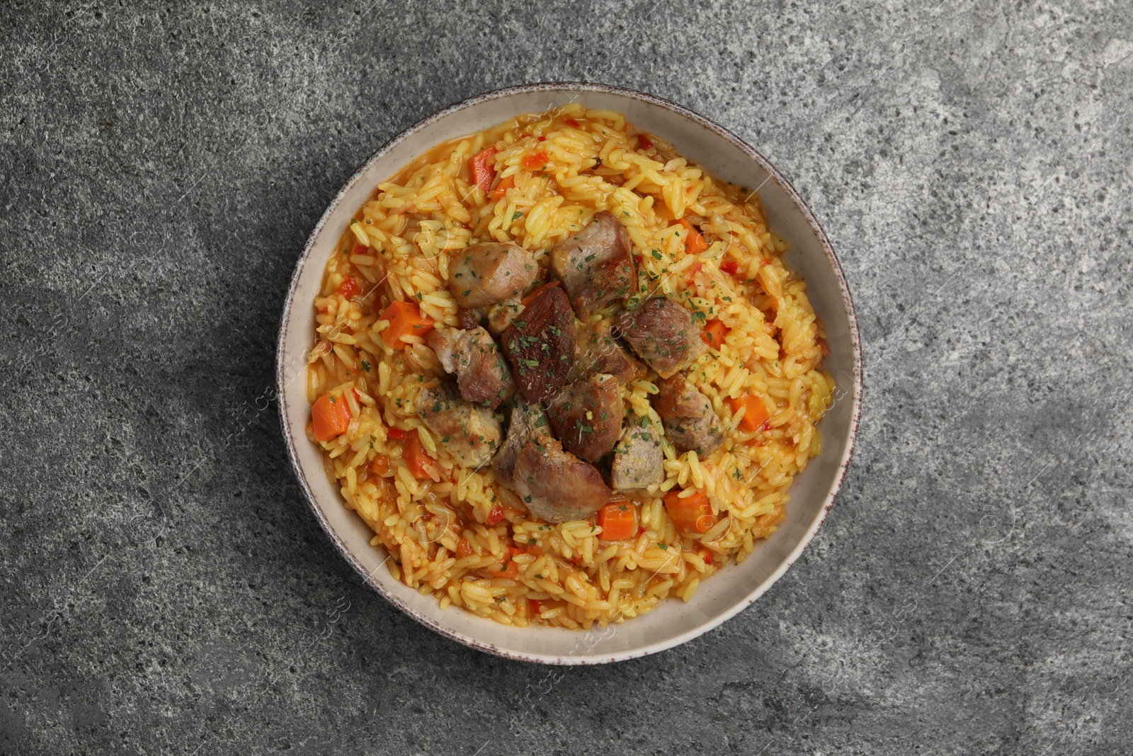 Photo of Delicious pilaf with meat on grey textured table, top view