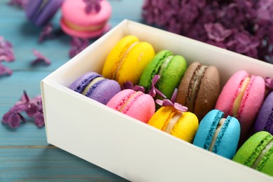 Delicious colorful macarons and flowers on light blue wooden table, closeup