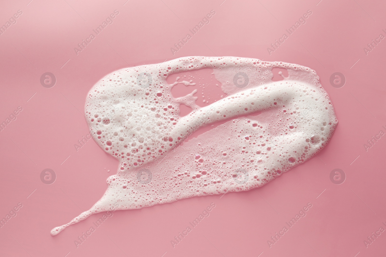 Photo of Smudge of white washing foam on pale pink background, top view