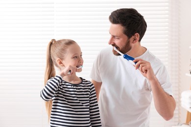 Photo of Father and his daughter brushing teeth together indoors