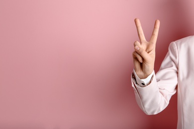 Young woman showing victory gesture on color background. Space for text