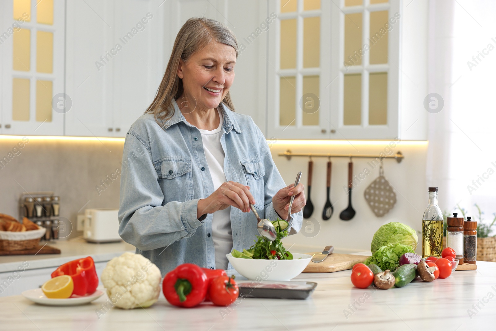 Photo of Happy woman making salad at table in kitchen