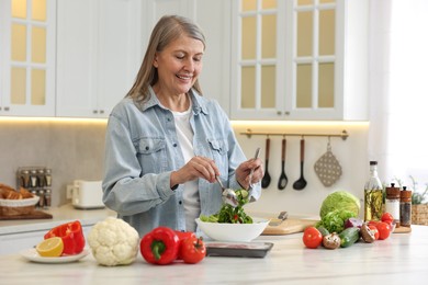 Happy woman making salad at table in kitchen