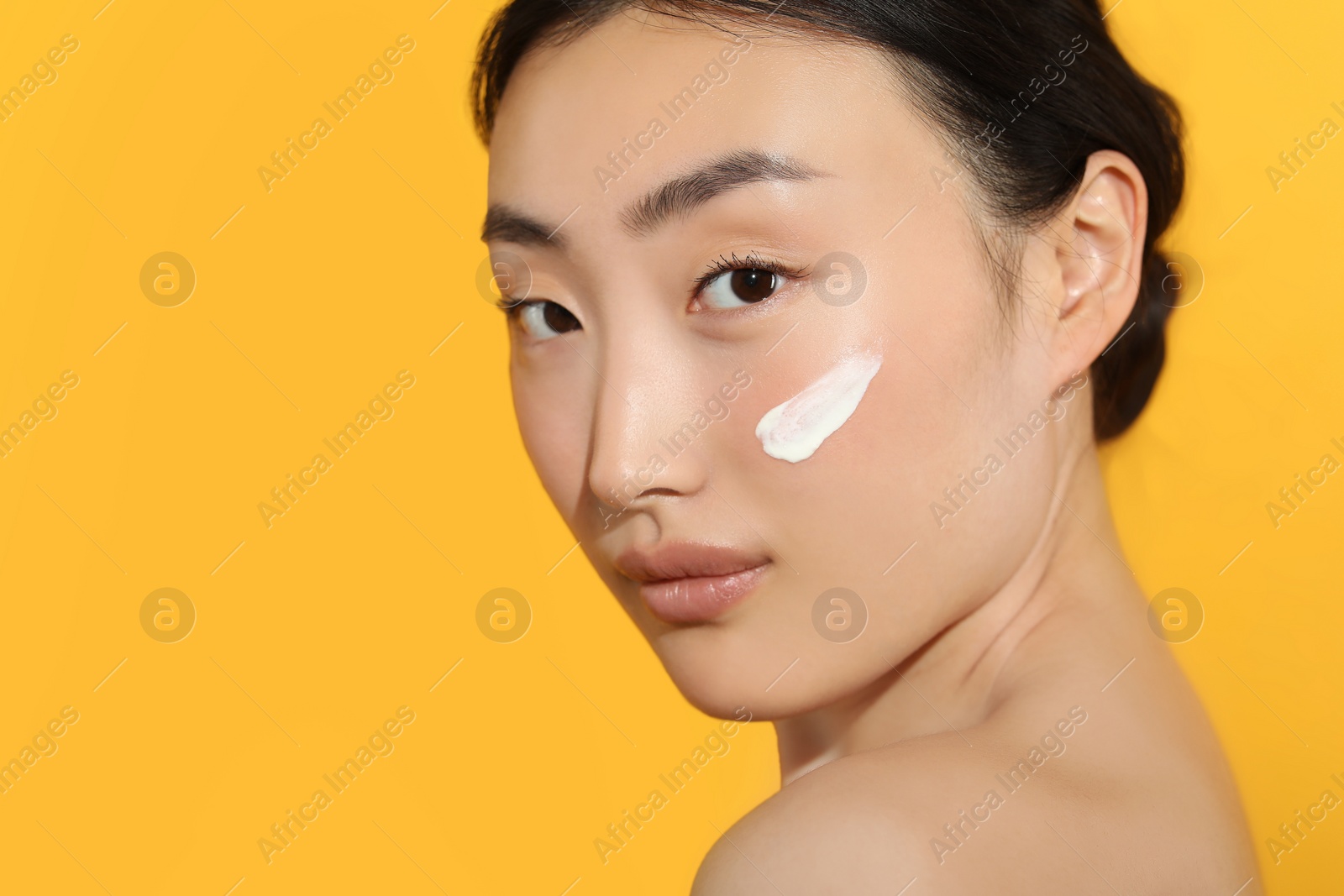 Photo of Beautiful young woman in sunlight with sun protection cream on her face against orange background, closeup. Space for text